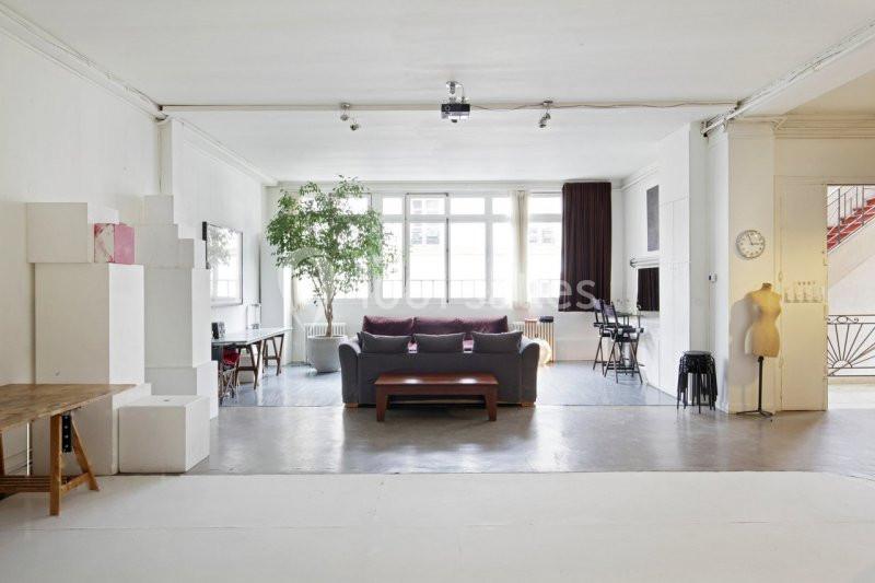 Espace lumineux avec canapé, table basse, plantes et mobilier minimaliste dans une pièce aux murs blancs.