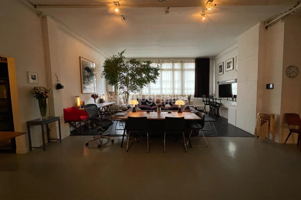 Espace intérieur lumineux avec grande table en bois, chaises noires, plantes, et mobilier moderne dans un cadre épuré.