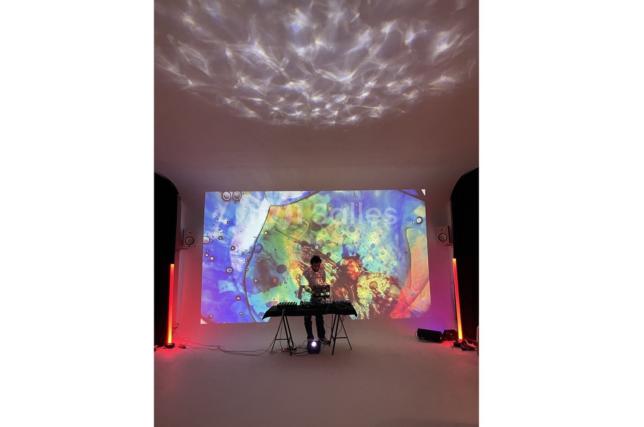 Un DJ mixe sur une table de sonorisation devant une projection colorée dans une pièce sombre.