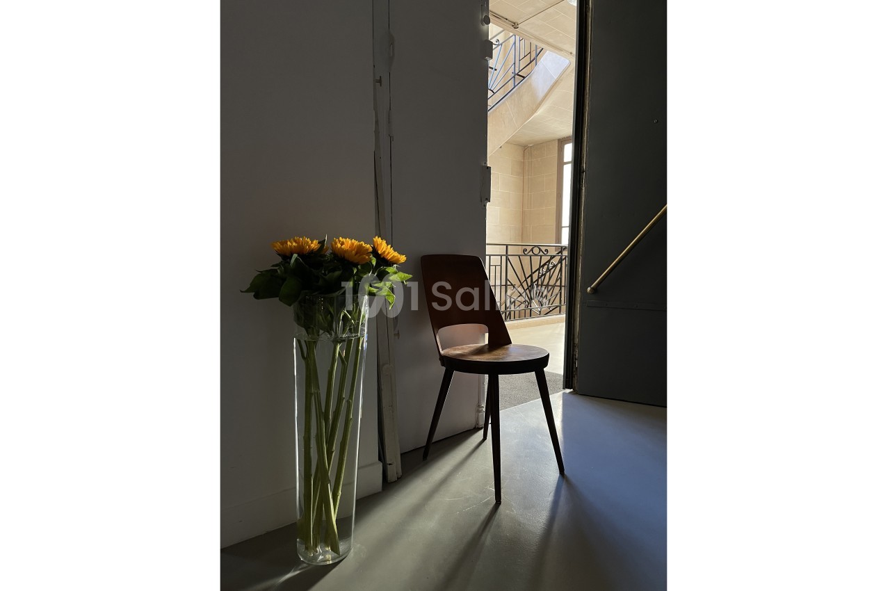 Vase de tournesols posé à côté d'une chaise en bois, éclairés par une lumière naturelle dans un intérieur minimaliste.