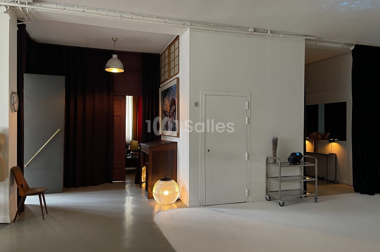 Espace intérieur avec murs blancs, rideaux sombres, mobilier minimaliste et éclairage tamisé.