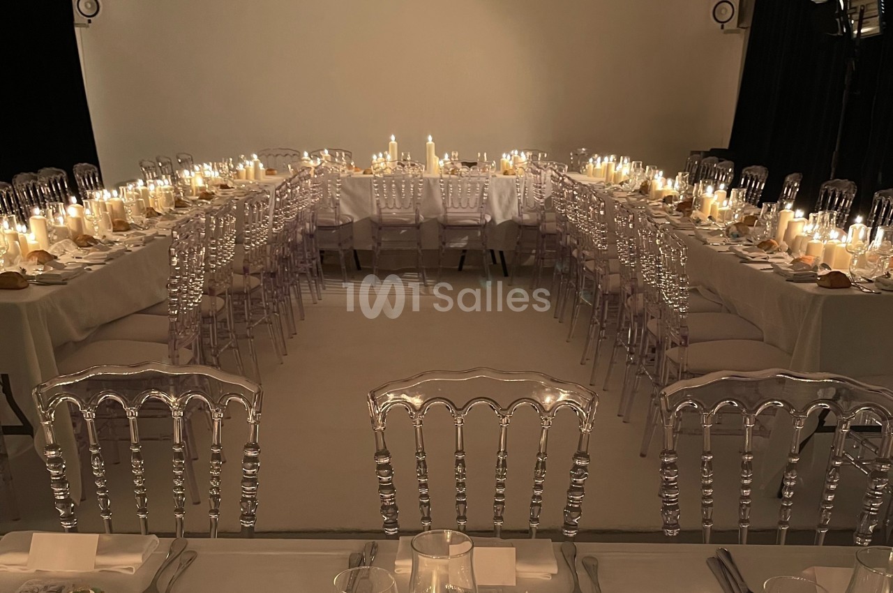 Salle de réception avec tables en U décorées de bougies, chaises transparentes et vaisselle élégante.