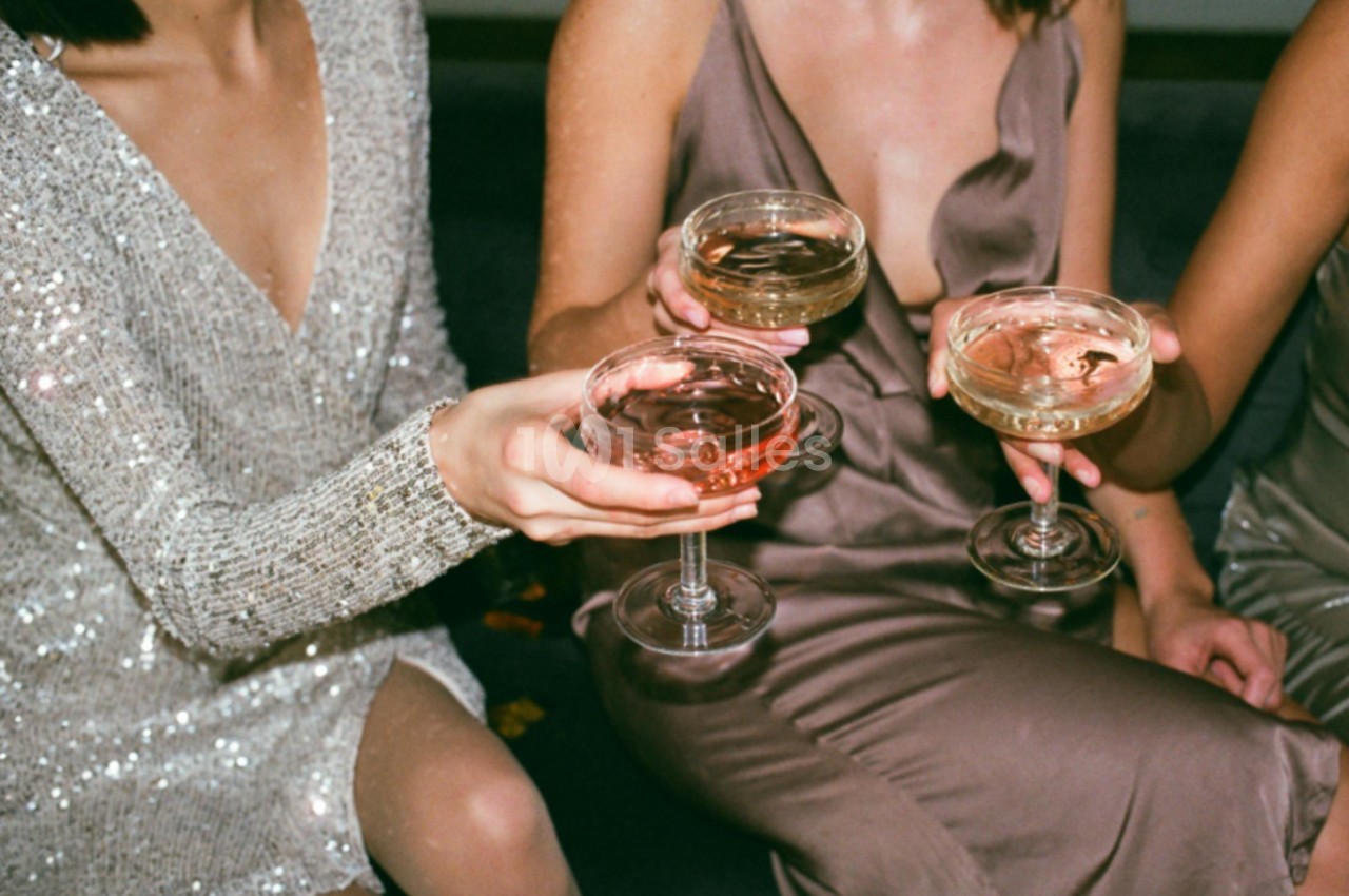 Trois personnes en tenue élégante trinquent avec des coupes de champagne remplies de boissons colorées.