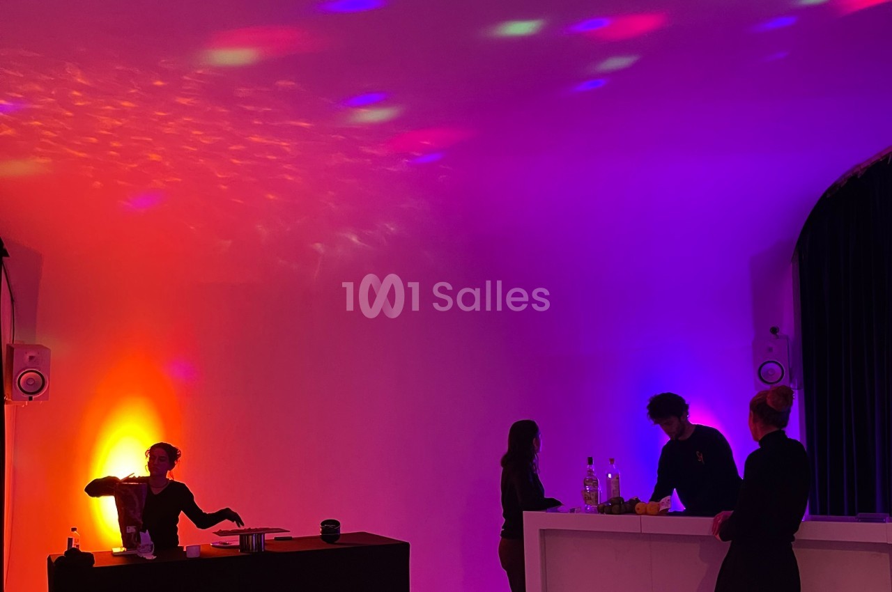 Quatre personnes dans un espace éclairé par des lumières colorées, avec un bar et une table en arrière-plan.