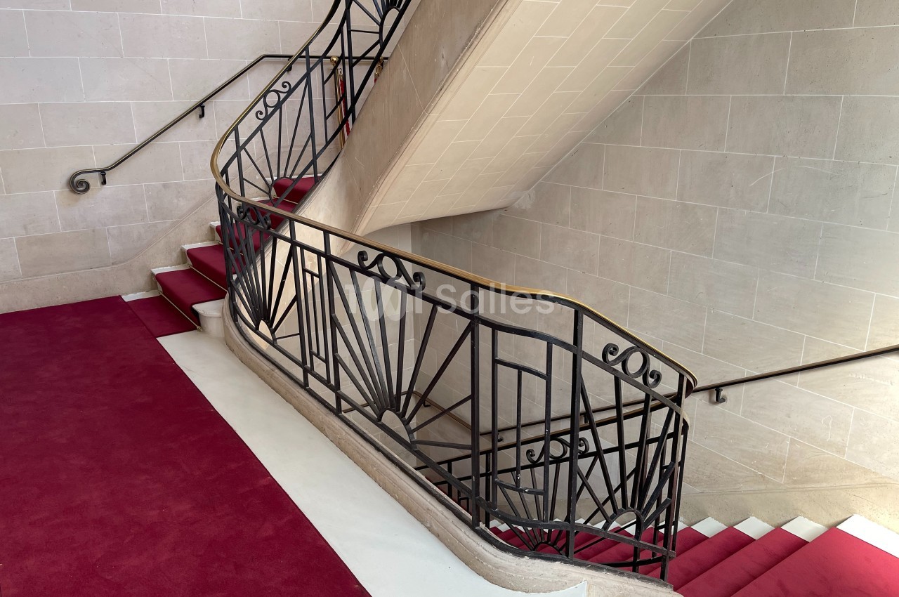 Escalier en pierre avec rampe en fer forgé de style Art déco et tapis rouge sur les marches.