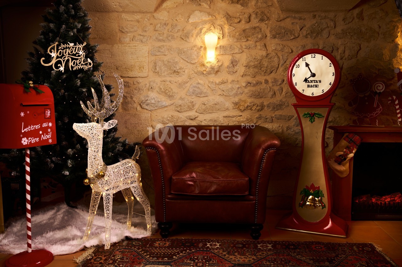 Fauteuil en cuir rouge entouré d'une décoration de Noël avec sapin, renne lumineux, boîte aux lettres et horloge vintage.