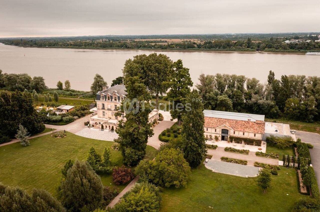 Vue aérienne d'un domaine avec un bâtiment principal, une dépendance, un jardin arboré et une rivière en arrière-plan.