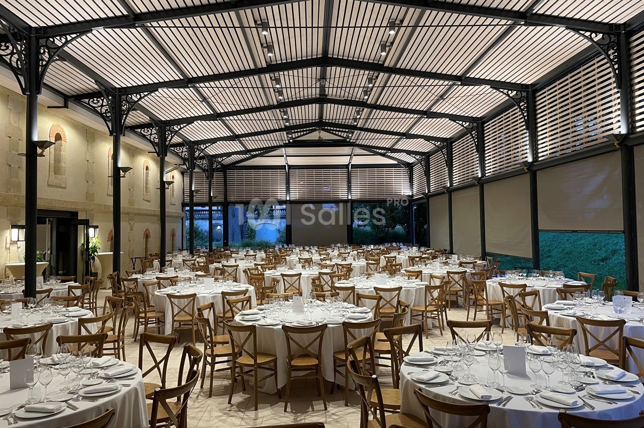 Salle de réception élégante avec tables rondes dressées, chaises en bois et toit en structure métallique ajourée.