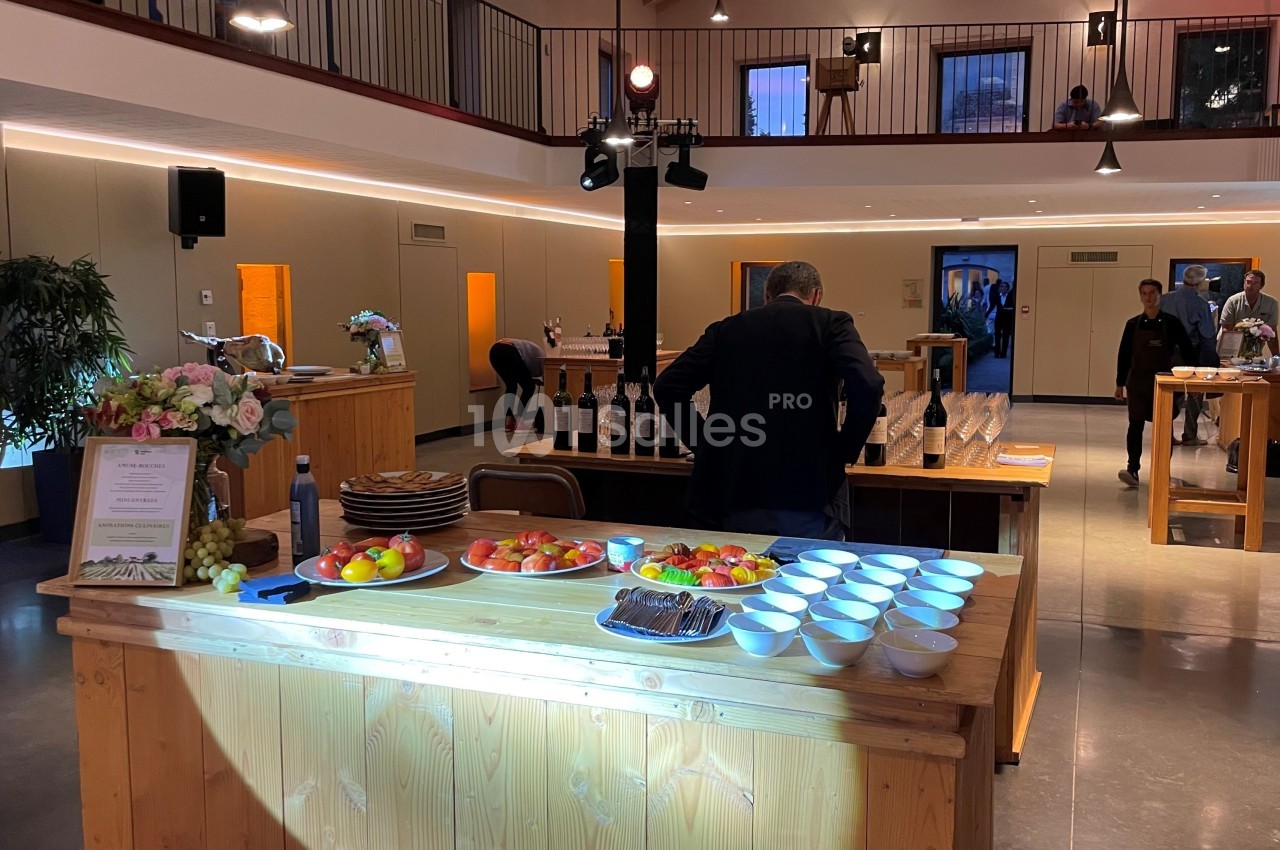 Salle lumineuse avec tables en bois, fruits, bols et bouteilles disposés pour un buffet ou une dégustation.