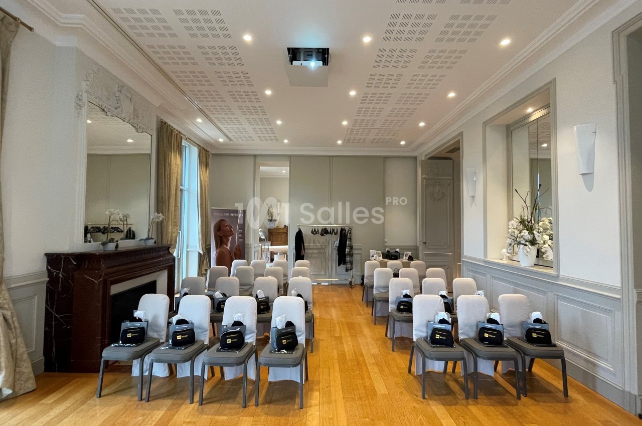 Salle de conférence lumineuse avec des rangées de chaises alignées, équipées de sacs noirs, et un écran de projection au…