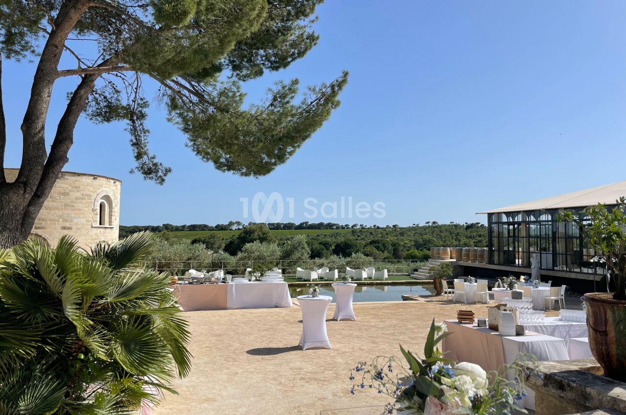 Terrasse ensoleillée avec tables dressées, vue sur un paysage verdoyant, une chapelle et une structure moderne.