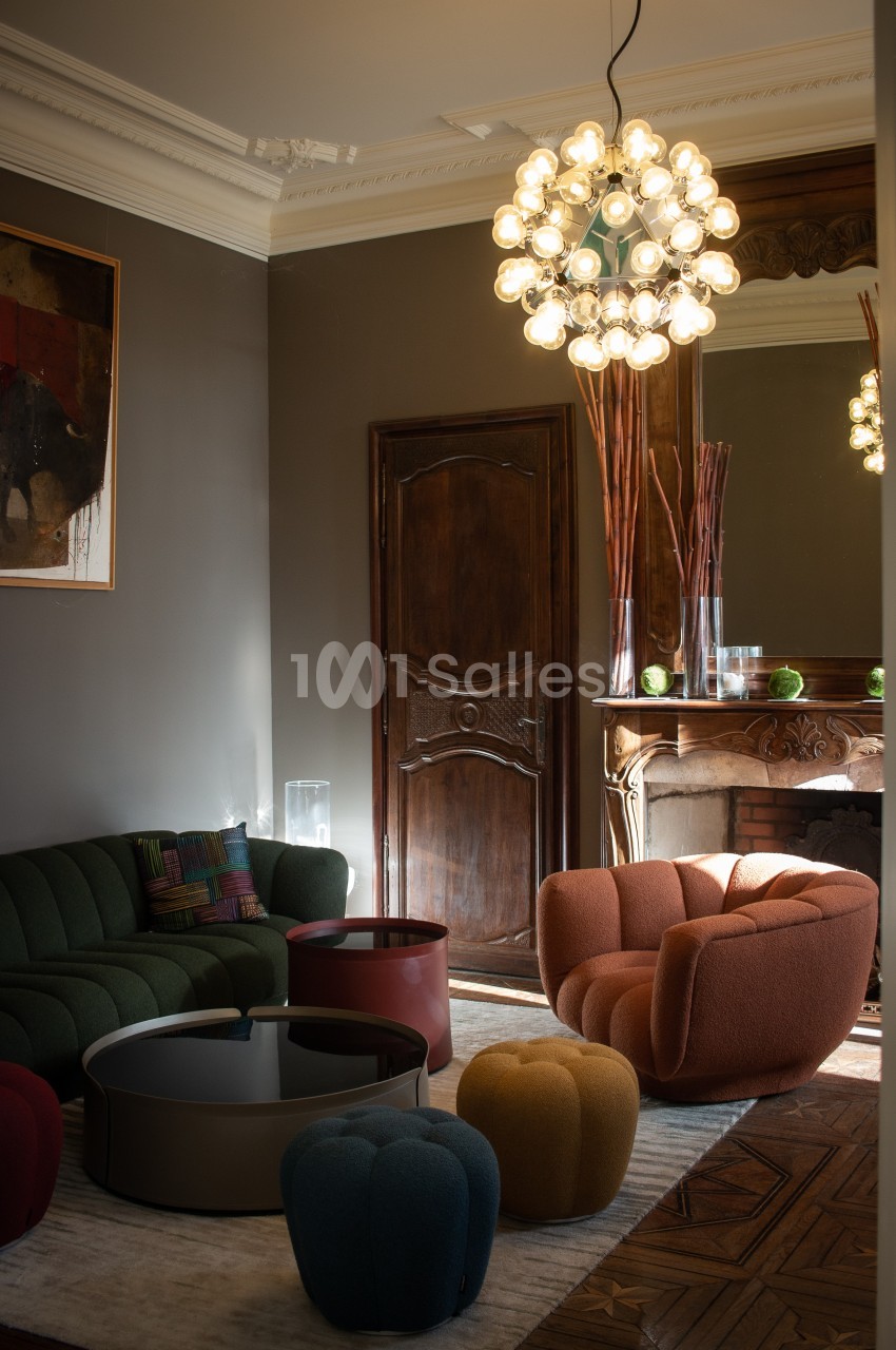 Salon élégant avec fauteuils colorés, table basse ronde, cheminée ornée et suspension lumineuse moderne.