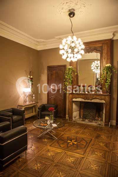 Salon élégant avec parquet à motifs, cheminée ornée de plantes, miroir ancien et mobilier contemporain.
