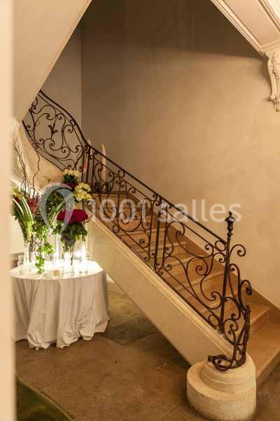 Escalier en pierre avec rampe en fer forgé décoratif, table ronde ornée de fleurs au pied de l'escalier.