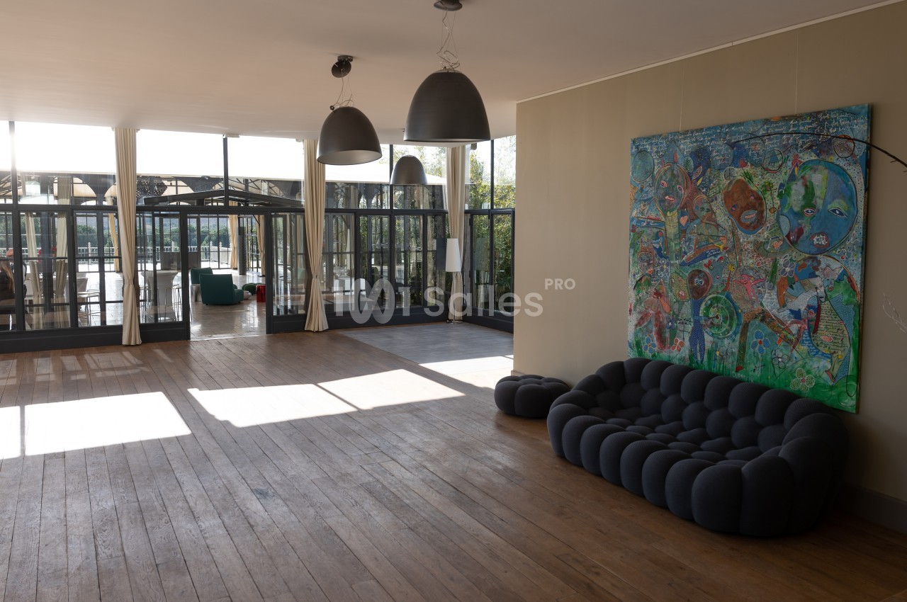Salle lumineuse avec parquet, canapé moderne, tableau coloré au mur et grandes baies vitrées donnant sur une terrasse.