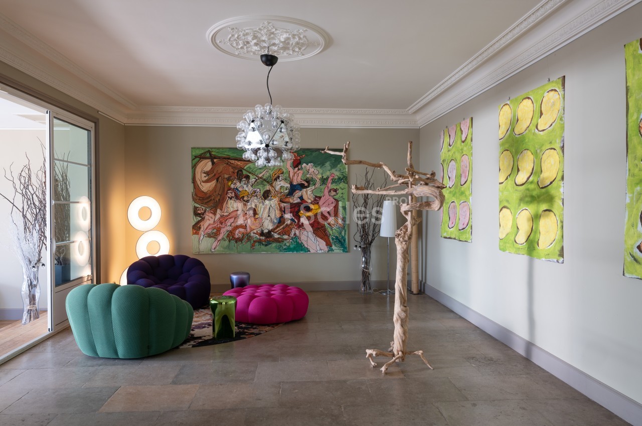 Salon moderne avec fauteuils colorés, œuvres d'art murales, lustre design et sculpture en bois sur un sol en pierre.