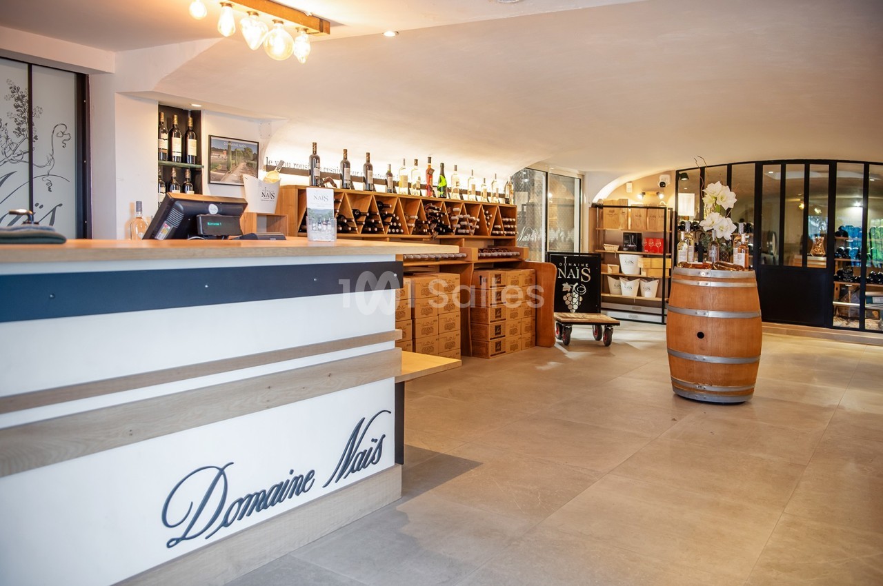Intérieur d'une cave à vin avec comptoir, étagères de bouteilles, tonneau en bois et décoration lumineuse.