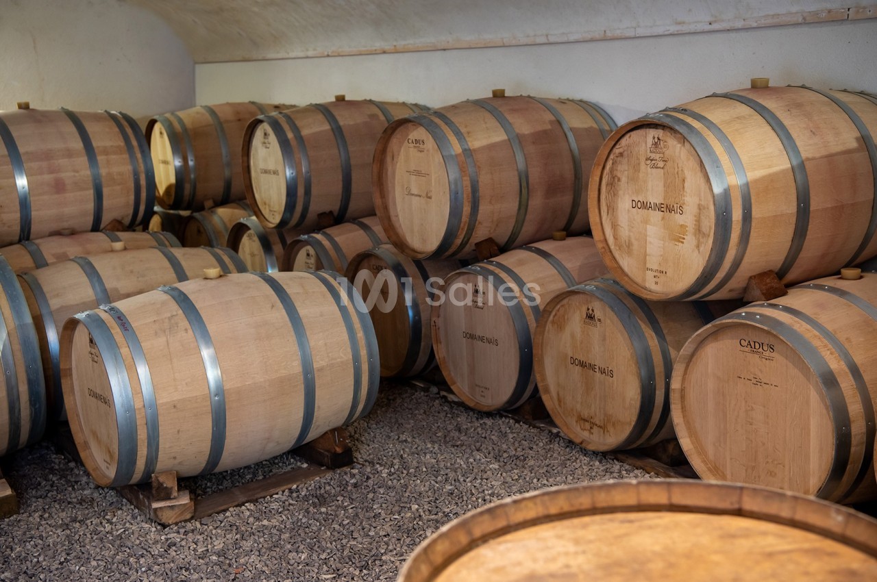 Fûts en bois alignés dans une cave, utilisés pour le vieillissement du vin.