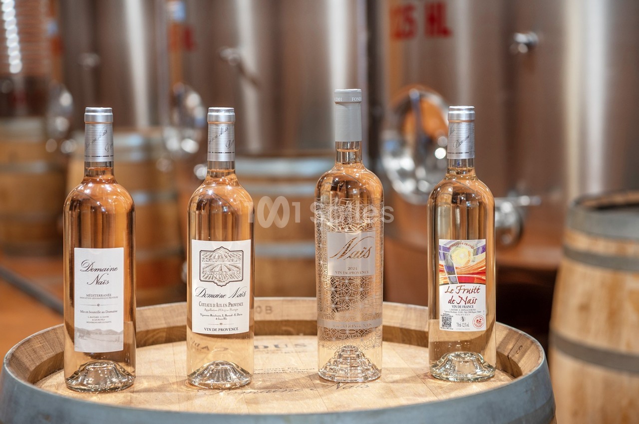 Quatre bouteilles de vin rosé posées sur un tonneau en bois, avec des cuves en acier en arrière-plan.