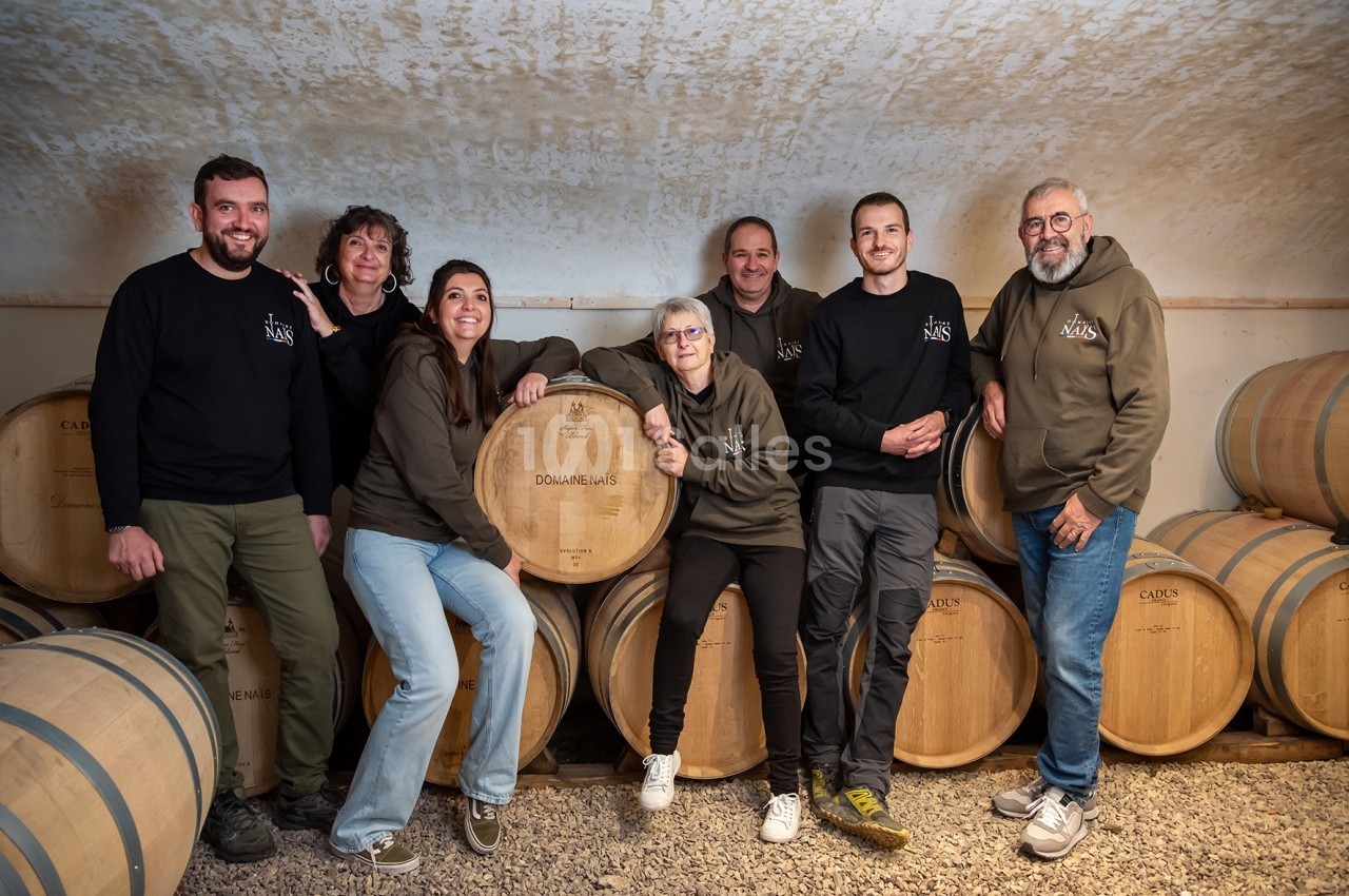Un groupe de personnes pose devant des fûts en bois dans une cave voûtée.