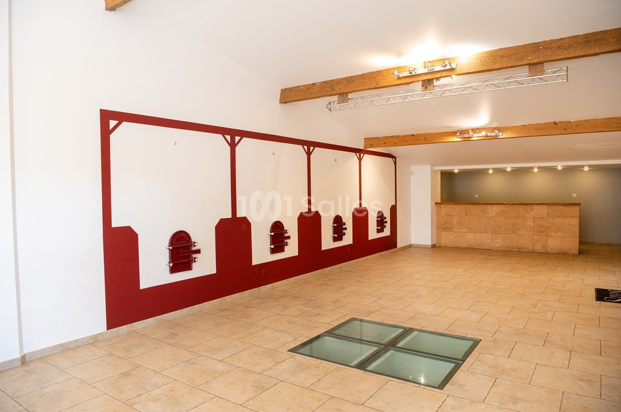 Salle lumineuse avec murs blancs, décorations rouges, sol en carrelage beige, comptoir en pierre et poutres apparentes.