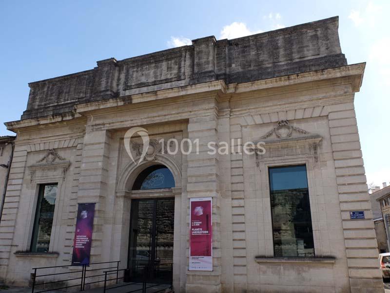 Façade d'un bâtiment en pierre avec une entrée centrale voûtée et des affiches sur les côtés.