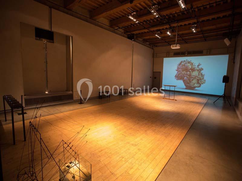 Salle d'exposition avec un sol en bois, des installations artistiques et une projection murale lumineuse.