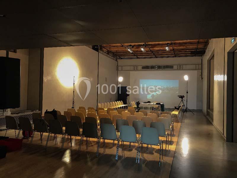 Salle de conférence vide avec des rangées de chaises, un projecteur allumé et un écran affichant une image.
