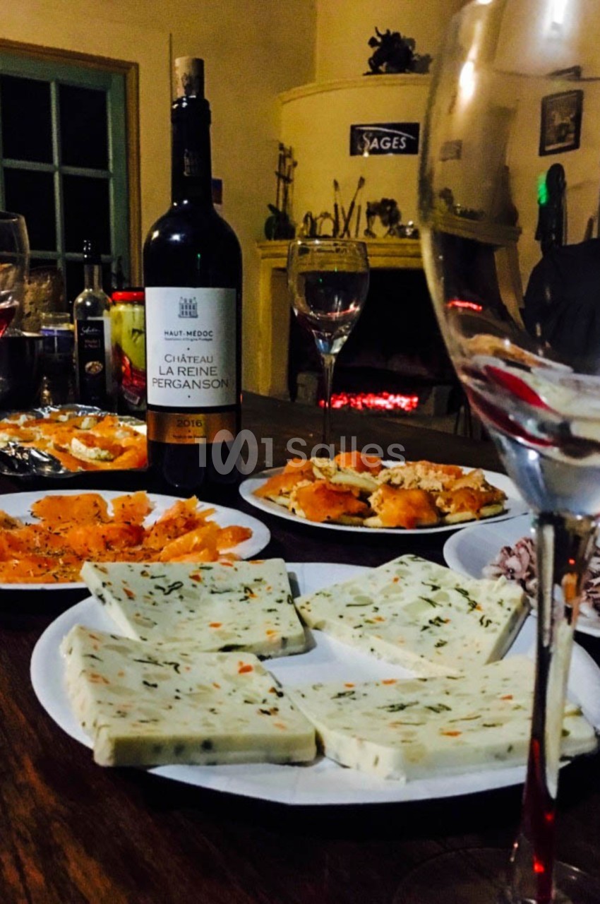 Assortiment de fromages et saumon fumé sur une table avec une bouteille de vin rouge, verres et cheminée en arrière-plan.
