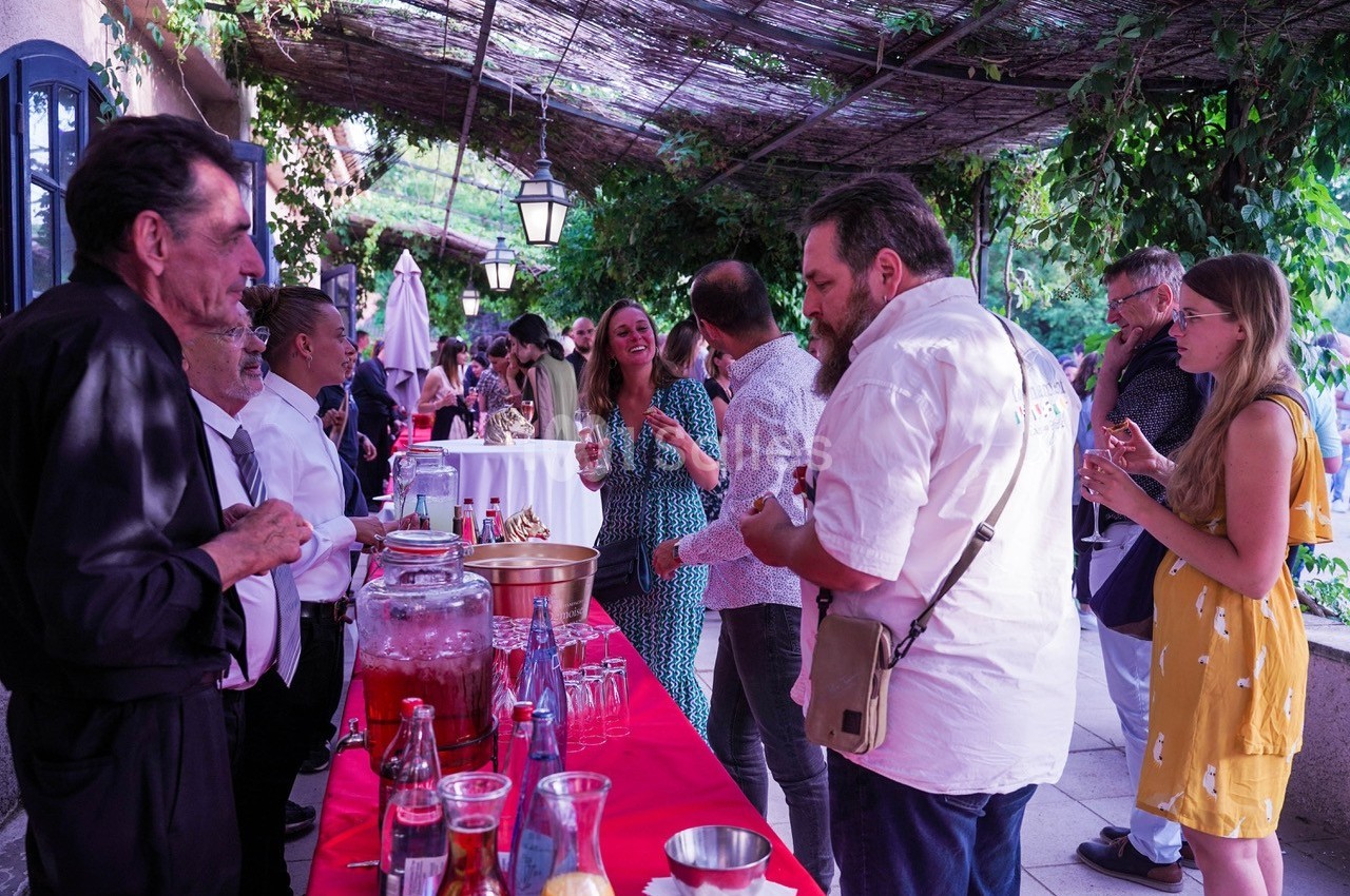 Groupe de personnes discutant et se servant à un buffet en extérieur sous une pergola ombragée.