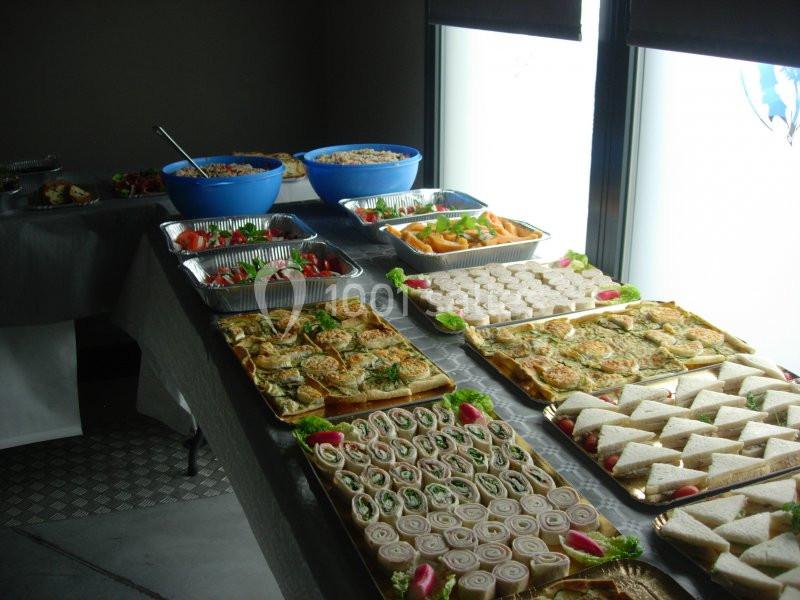 Buffet avec divers plats froids, incluant sandwichs, roulés, salades et quiches, disposés sur une table.