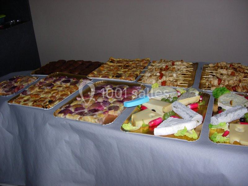 Plateaux variés de nourriture comprenant quiches, brochettes, fromages et charcuteries sur une table couverte.