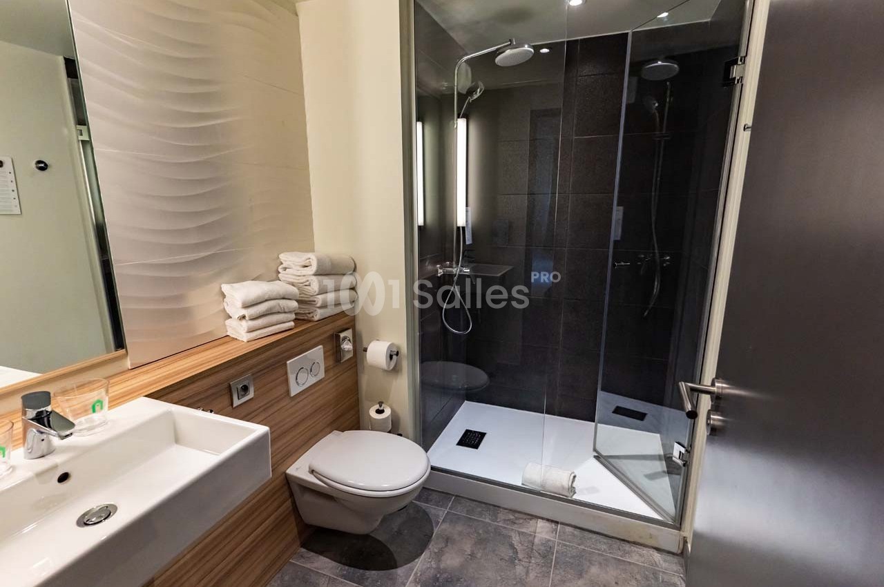 Salle de bain moderne avec douche vitrée, lavabo, toilettes et serviettes pliées sur un plan de travail en bois.