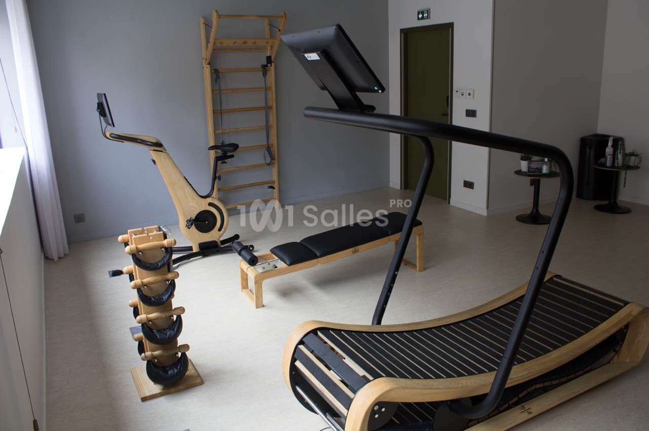 Salle de sport équipée d'un tapis de course en bois, d'un vélo d'exercice, d'haltères et d'un espalier.