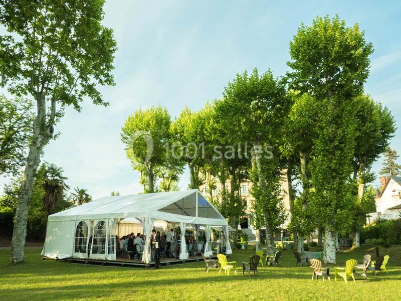 Tente blanche installée sur une pelouse entourée d'arbres, avec des chaises dispersées à l'extérieur.