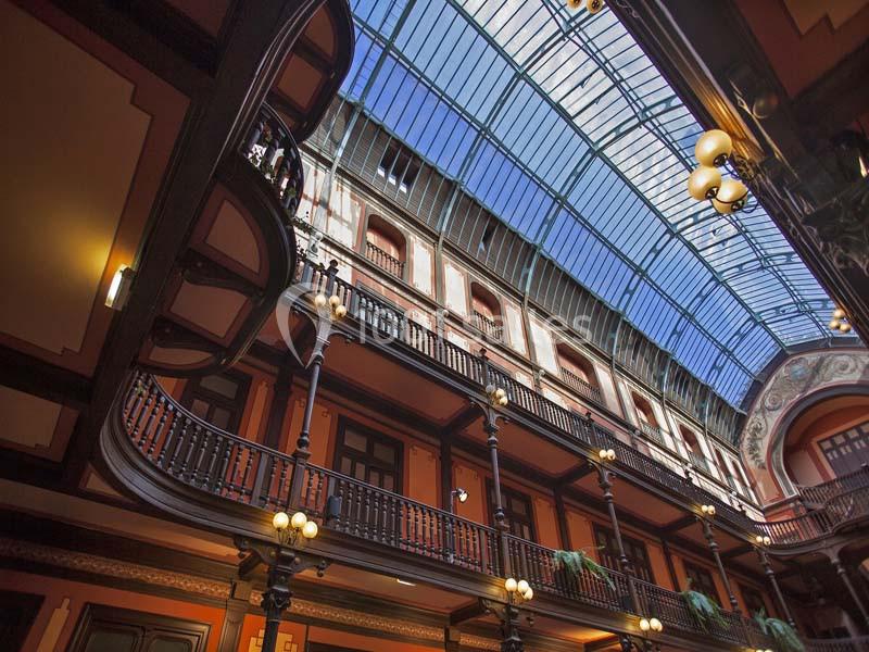 Vue intérieure d'un bâtiment avec une verrière, des balustrades en bois et des lampes suspendues.
