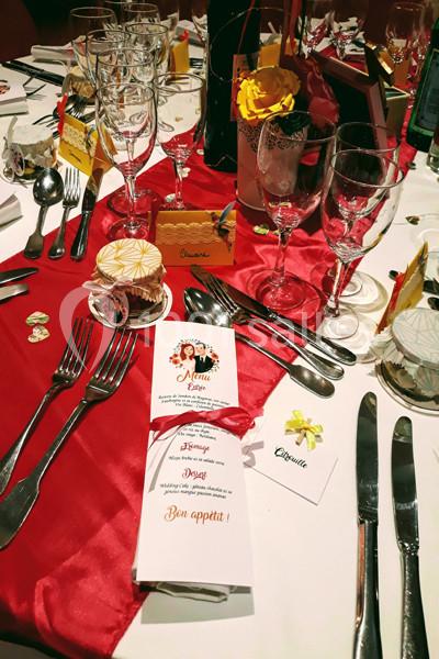 Table dressée pour un repas festif avec menus, couverts, verres, décorations colorées et cadeaux invités.