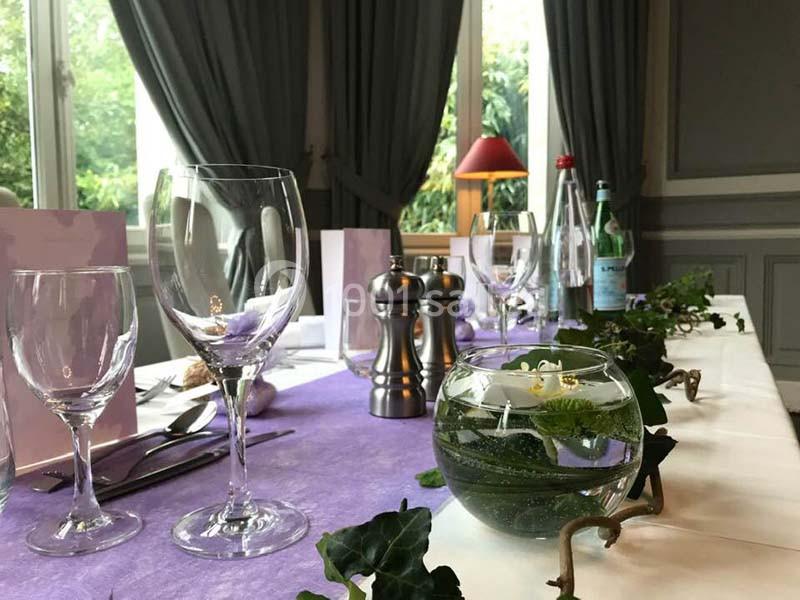 Table élégamment dressée avec nappes violettes, verres, couverts, décoration végétale et carafes d'eau.