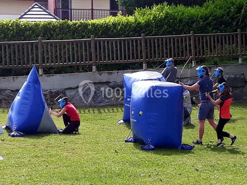 Des personnes jouent à un jeu d'archerie avec des arcs et des flèches en mousse, abritées derrière des structures gonflables.