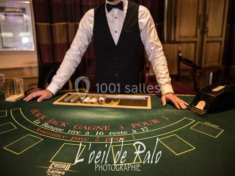 Croupier debout derrière une table de blackjack dans un casino, avec jetons et cartes visibles.