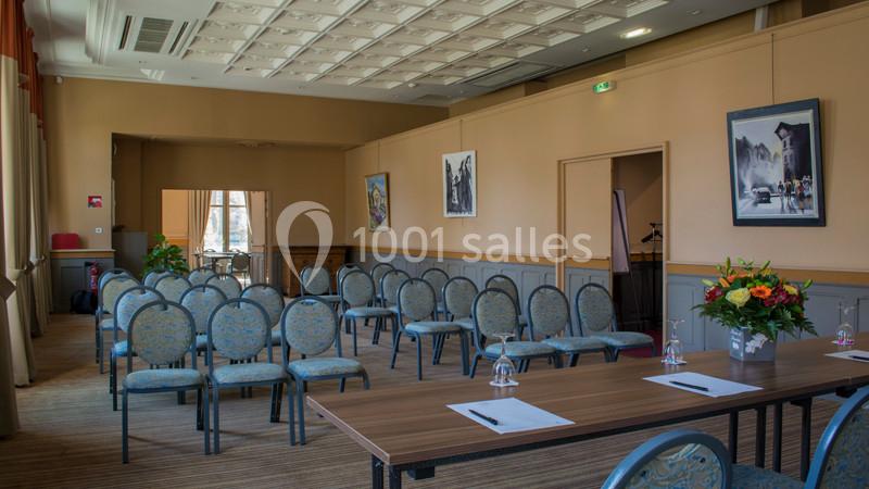 Salle de réunion lumineuse avec chaises alignées, tables équipées de verres et stylos, et décorations murales.