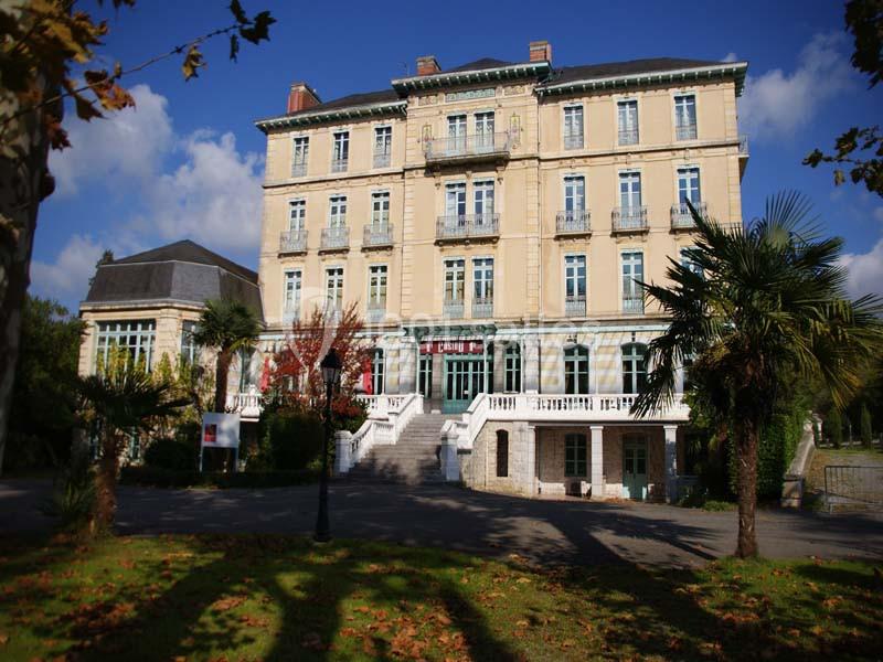 Façade d'un bâtiment ancien à plusieurs étages, entouré de palmiers et d'arbres sous un ciel dégagé.