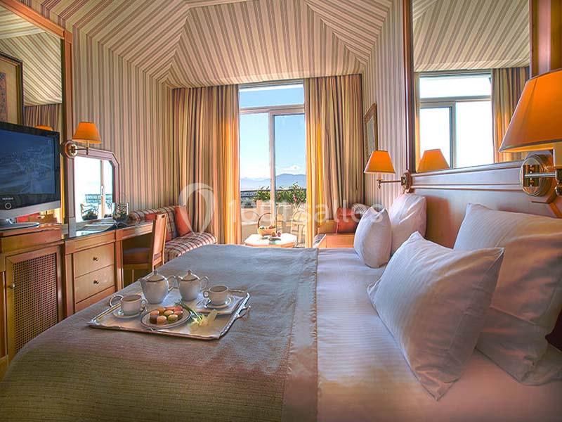 Chambre d'hôtel lumineuse avec lit double, plateau de thé, bureau, téléviseur et vue sur un paysage extérieur.