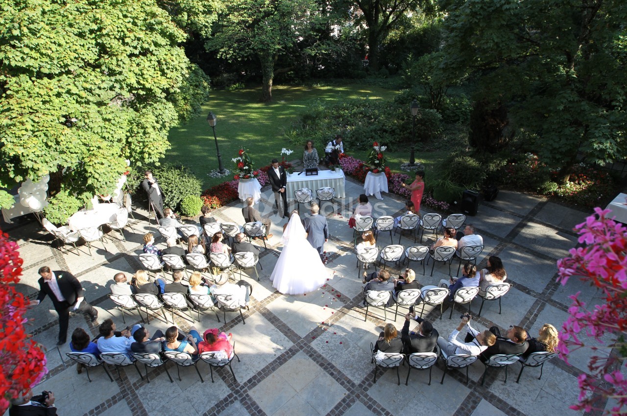Cérémonie de mariage en plein air avec des invités assis, vue depuis le dessus, entourée de verdure et de fleurs.