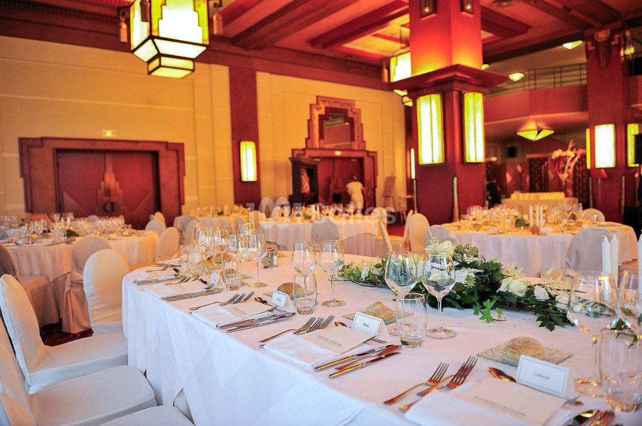 Salle de réception élégante avec tables dressées, nappes blanches, verres, couverts et décoration florale.