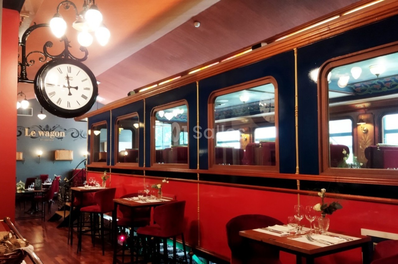 Salle de restaurant décorée comme un wagon de train, avec tables dressées et horloge murale rétro.
