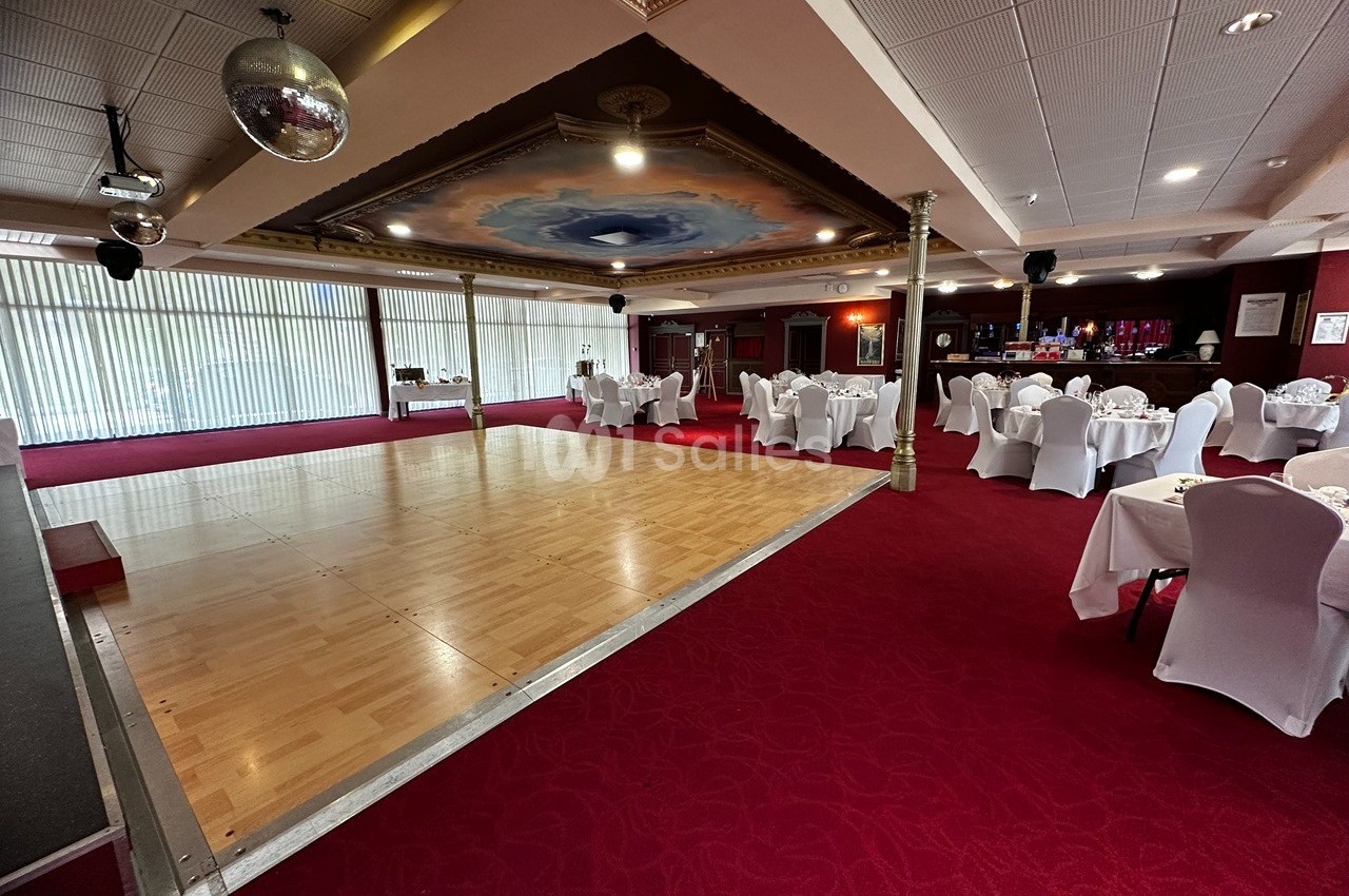 Salle de réception avec parquet pour danse, tables dressées avec nappes blanches et plafond décoré.