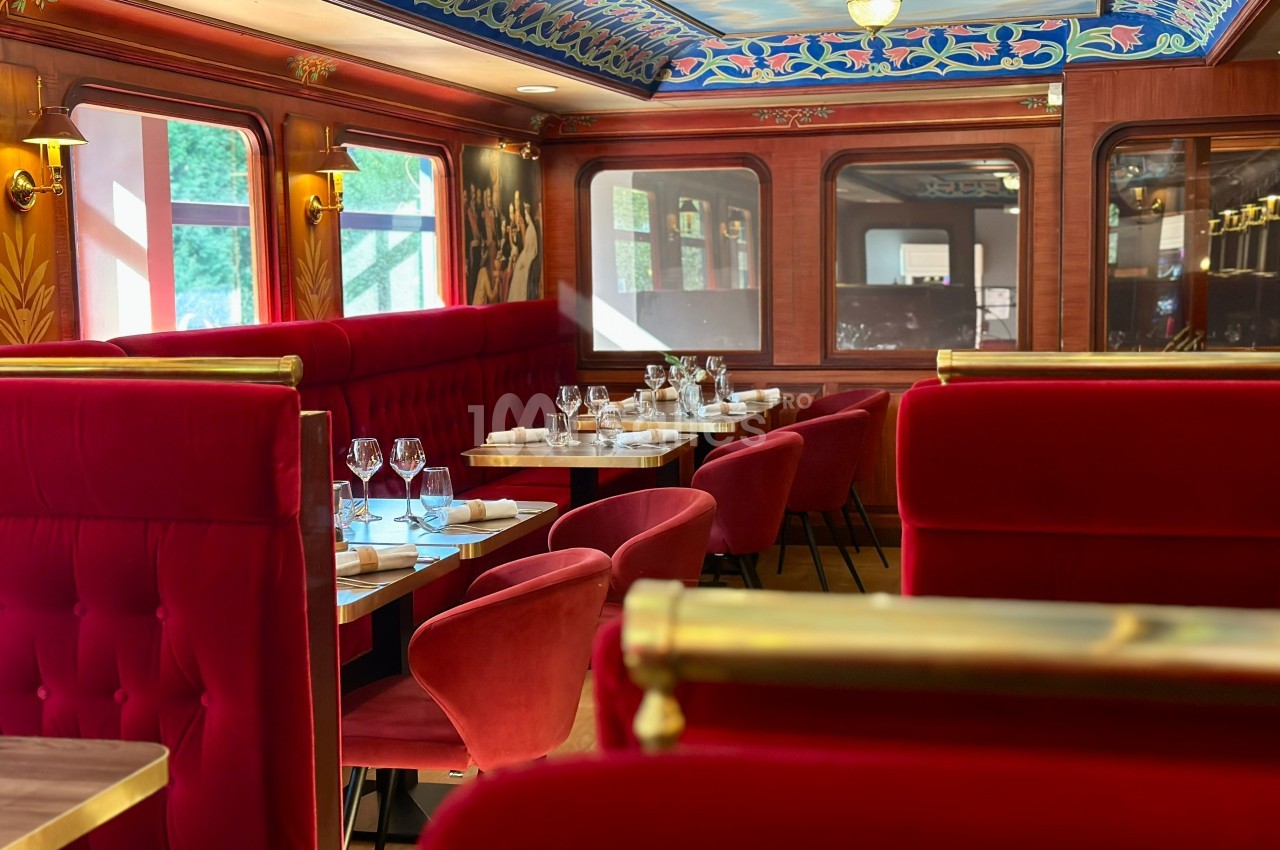 Salle de restaurant élégante avec banquettes rouges, tables dressées et décorations murales raffinées.