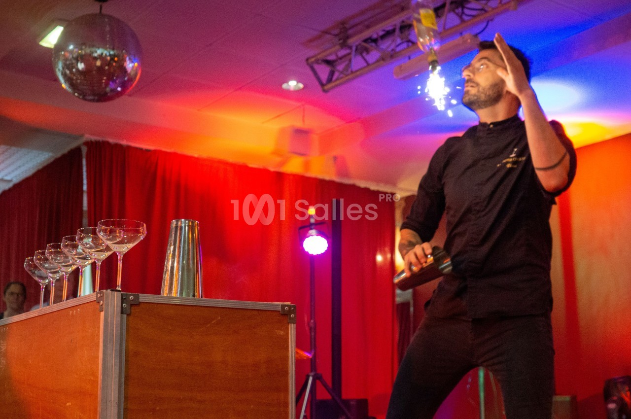 Un barman réalise un spectacle de flair bartending avec des verres et un shaker dans une salle éclairée.