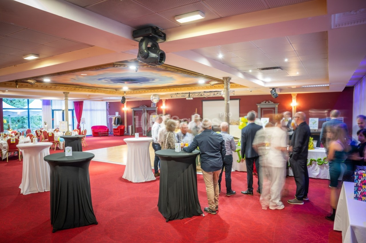 Personnes rassemblées dans une salle de réception avec tables hautes, éclairage chaleureux et décorations élégantes.